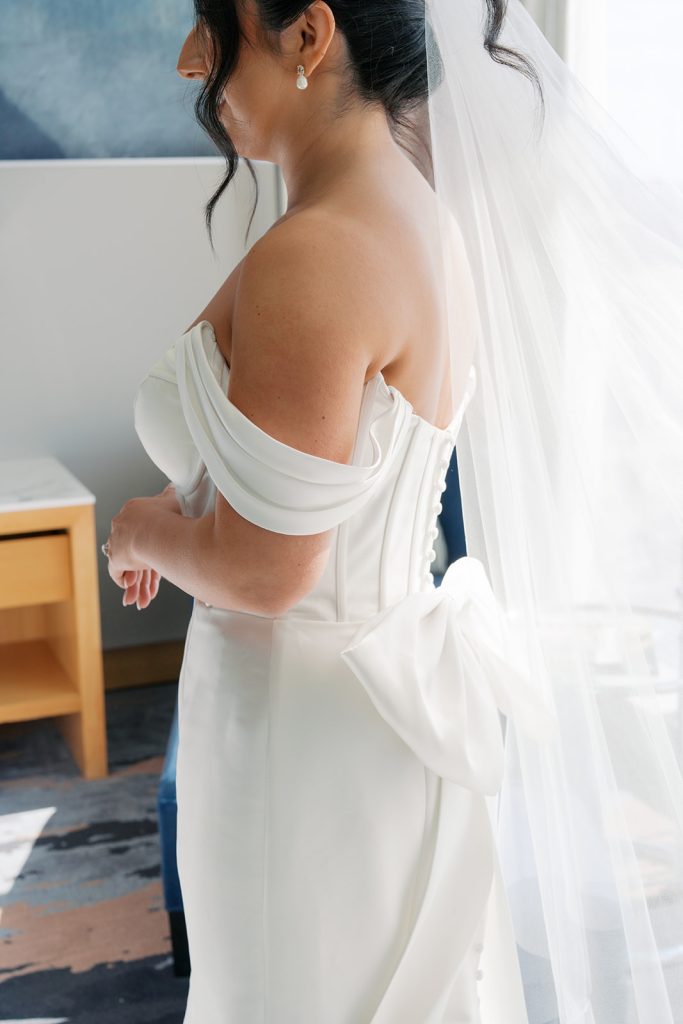 Close-up of Katie's off-shoulder wedding gown featuring draped sleeves and elegant pearl drop earrings