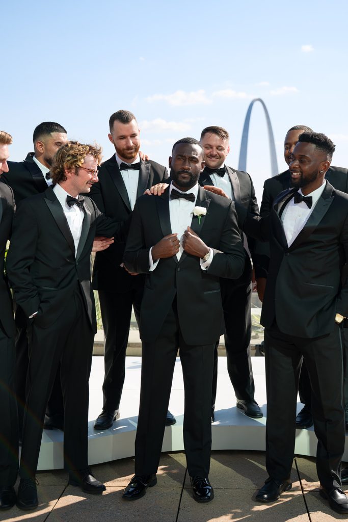 Anthony and groomsmen in black tuxedos on rooftop, Gateway Arch in background