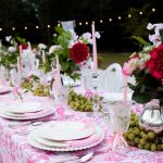 Evening wedding reception table with pink linens, illuminated by string lights and decorated with red and pink flowers