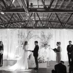 Industrial venue wedding ceremony with exposed beams, string lights, and modern Sofreh Aghd backdrop