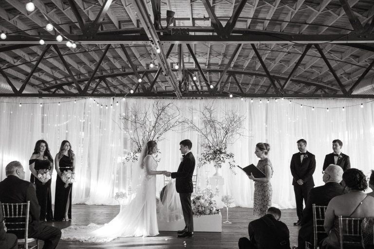 Industrial venue wedding ceremony with exposed beams, string lights, and modern Sofreh Aghd backdrop