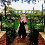 Wedding officiant in black dress standing in formal garden venue with ornamental iron gates