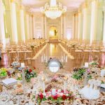 Elegant Persian Sofreh Aghd ceremony spread in grand ballroom with ornate chandelier, gold chiavari chairs, mirror, candles, nuts, and rose petals