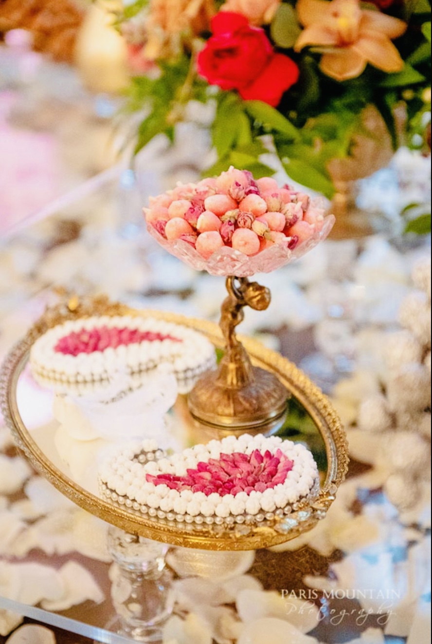 Traditional Persian Sofreh Aghd display with gold tiered stands, decorated sweets, and pink floral accents