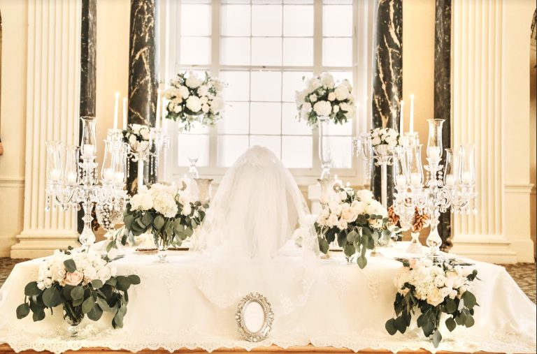 Elegant Sofreh Aghd setup with white draping, tall candelabras, and ivory floral arrangements