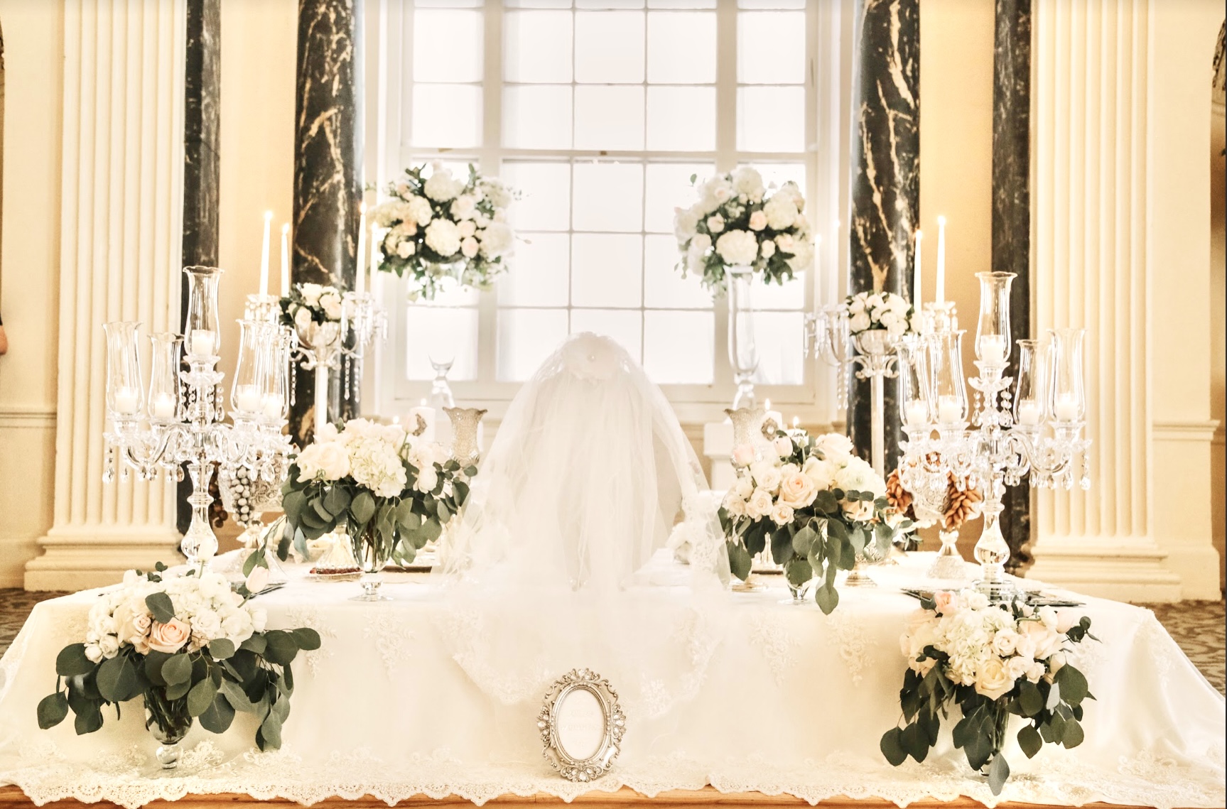 Elegant Sofreh Aghd setup with white draping, tall candelabras, and ivory floral arrangements