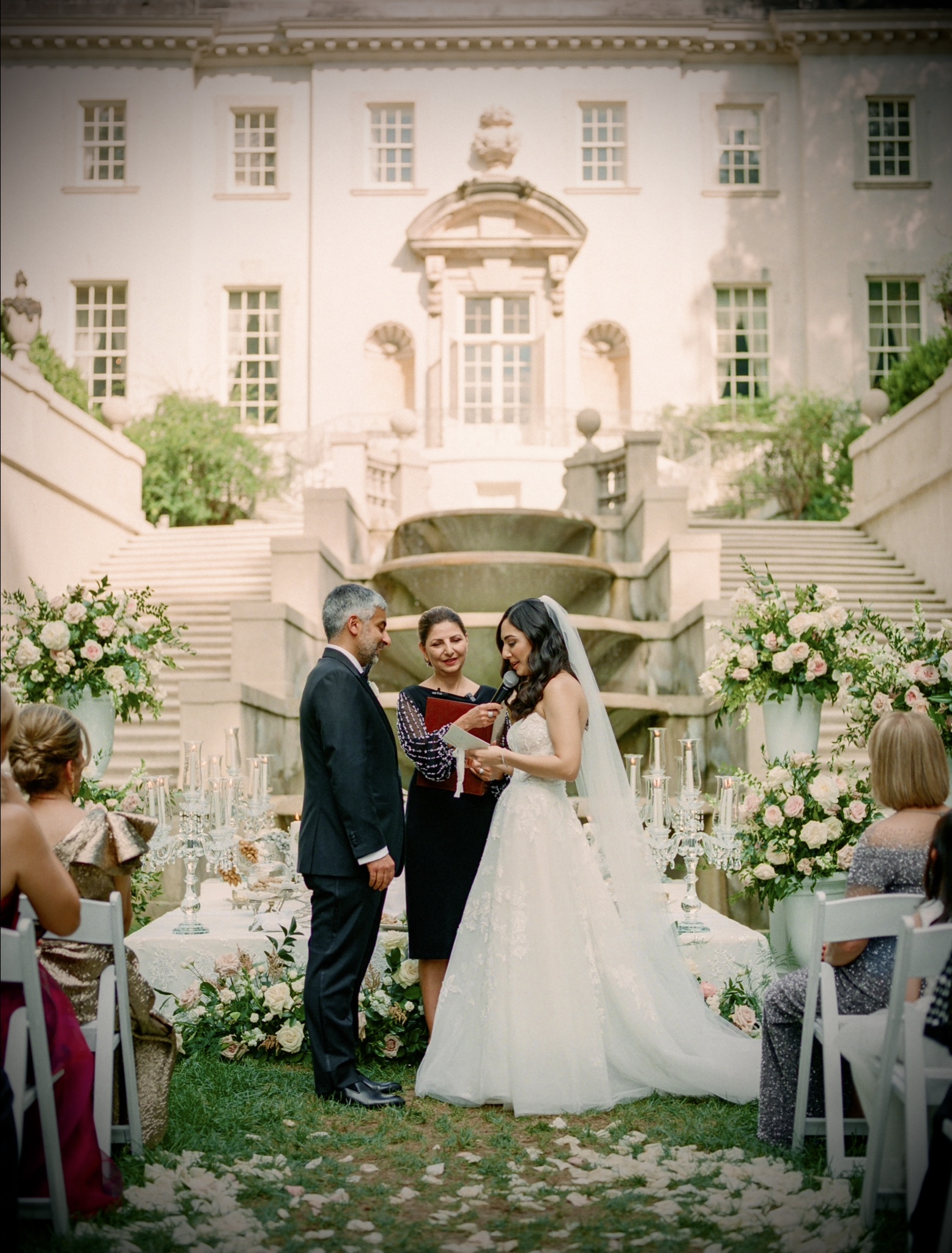 Persian wedding ceremony at grand estate with lush greenery, white floral displays, and seated guests
