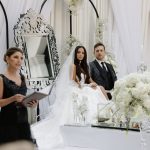 Bride and groom seated at white Sofreh Aghd ceremony table with officiant