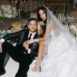 Bride and groom seated at traditional Sofreh Aghd with ornate floral backdrop and Persian ceremonial elements