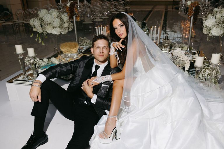 Bride and groom seated at traditional Sofreh Aghd with ornate floral backdrop and Persian ceremonial elements