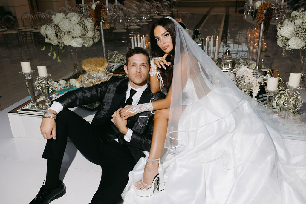 Bride and groom seated at traditional Sofreh Aghd with ornate floral backdrop and Persian ceremonial elements