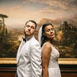 Bride and groom posed back-to-back in front of classical landscape painting at art museum