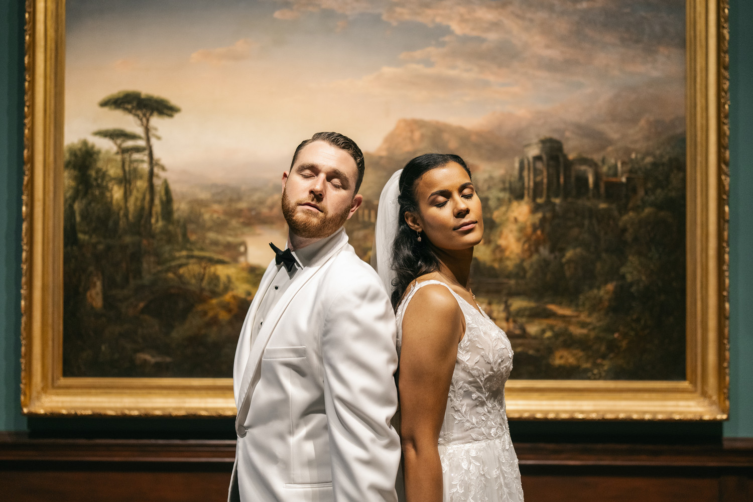 Bride and groom posed back-to-back in front of classical landscape painting at art museum