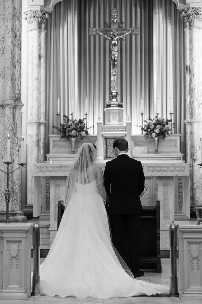 Bride and groom kneeling at church altar beneath crucifix during their wedding ceremony