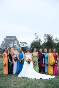 Bride in white gown with bridesmaids in rainbow-colored dresses holding autumn bouquets at St. Louis botanical garden