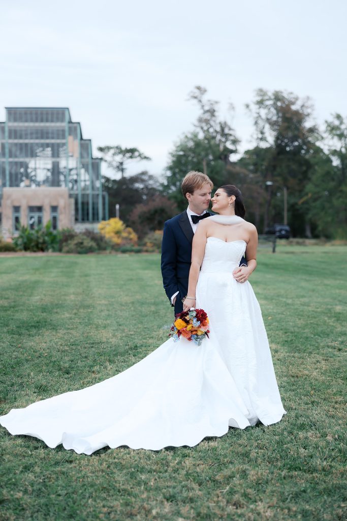 Caroline and Josh pose in botanical garden with bride's cathedral-length train spread across lawn