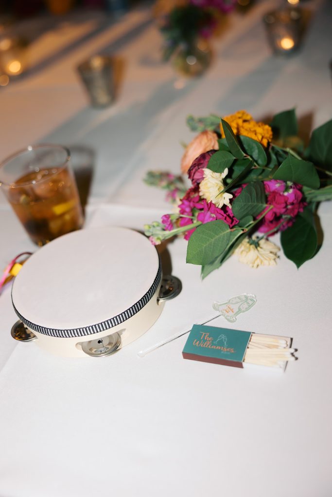 Wedding reception table detail featuring tambourine, colorful floral arrangement, and matchbook favors