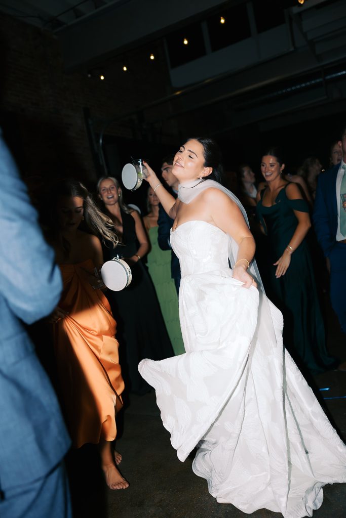 Caroline dances energetically with tambourine while wedding guests celebrate around her on reception dance floor
