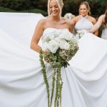 Bride holding oversized white and green bouquet with cascading amaranthus while bridesmaids look on