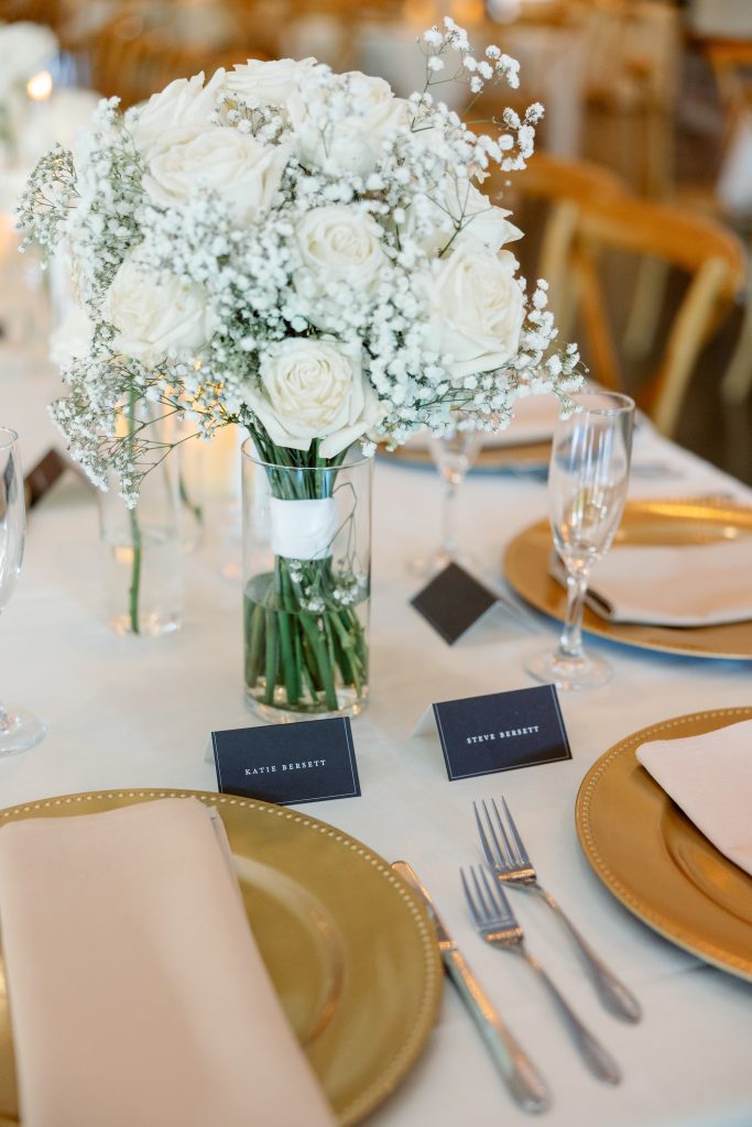 White rose and baby's breath centerpiece with gold place settings and black name cards
