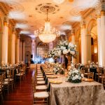 Grand ballroom with crystal chandeliers, ornate ceiling, and white floral arrangements