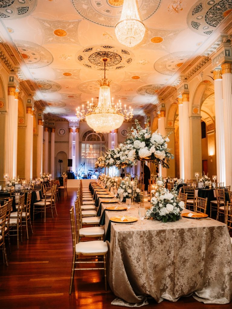 Grand ballroom with crystal chandeliers, ornate ceiling, and white floral arrangements