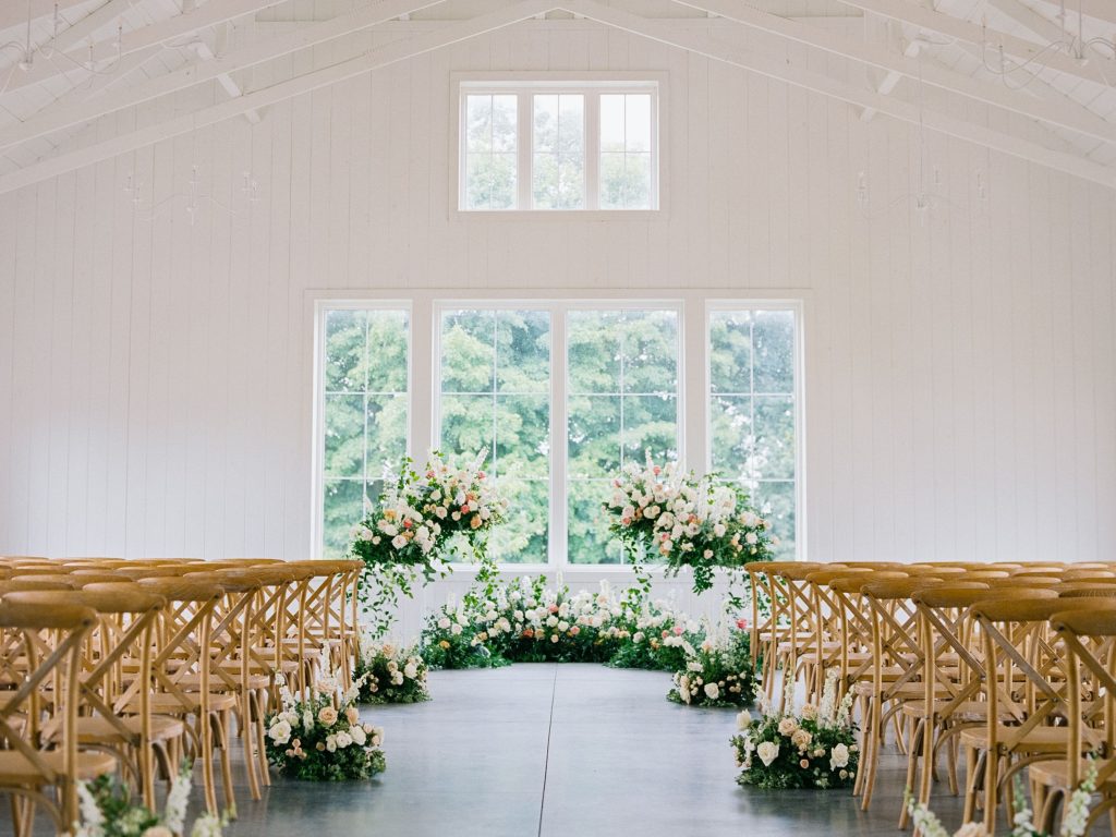 White barn wedding ceremony space with wood chairs arranged in rows and floral arrangements lining the aisle