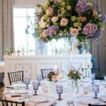 Tall centerpiece with purple hydrangeas, blush roses, and green blooms on elegant reception table