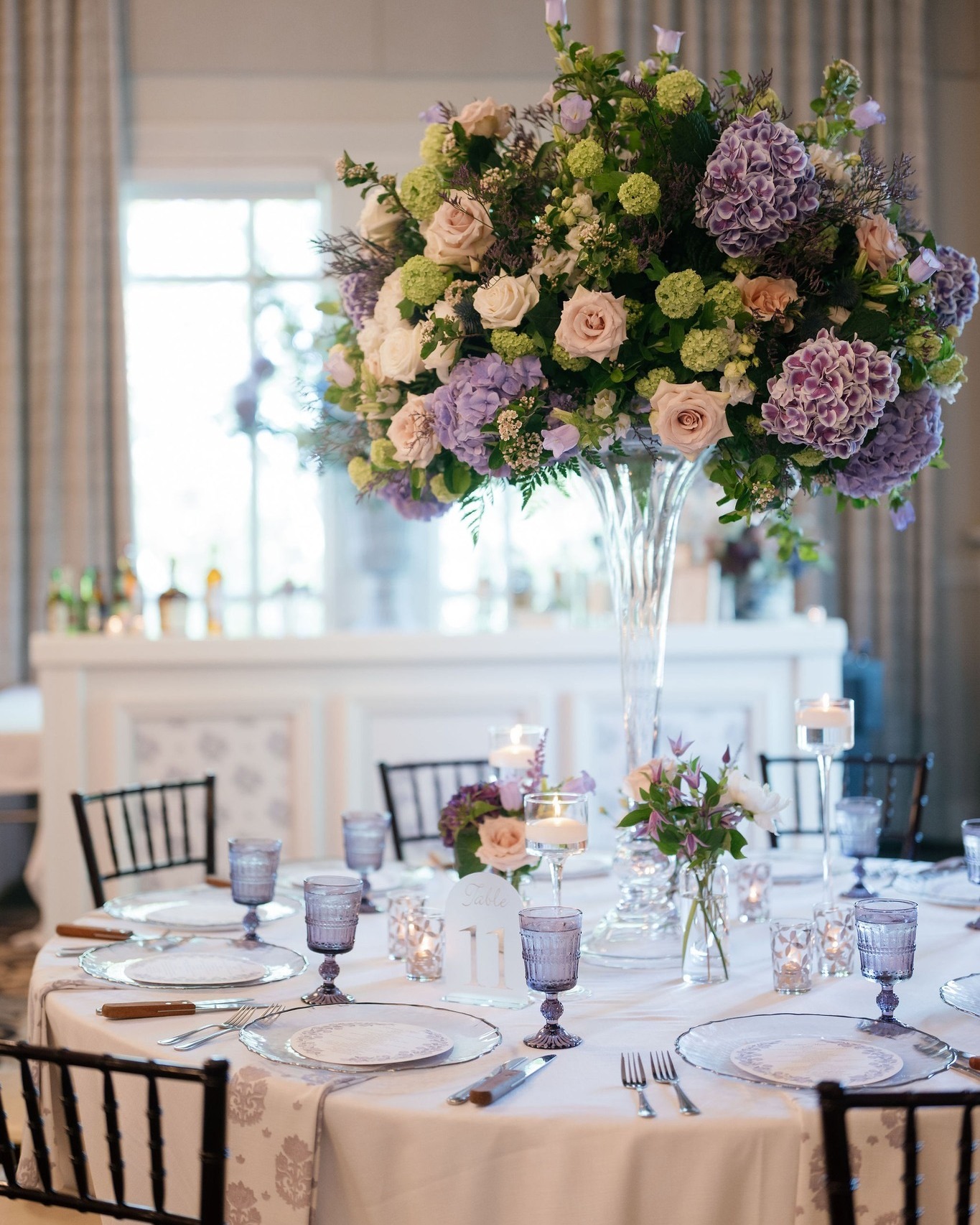 Tall centerpiece with purple hydrangeas, blush roses, and green blooms on elegant reception table