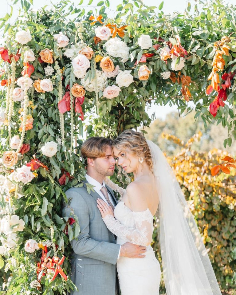 Couple kissing beneath vibrant floral arch featuring orange, pink, and white blooms