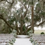 Southern wedding ceremony setup with white hydrangea florals along aisle under moss-covered oaks