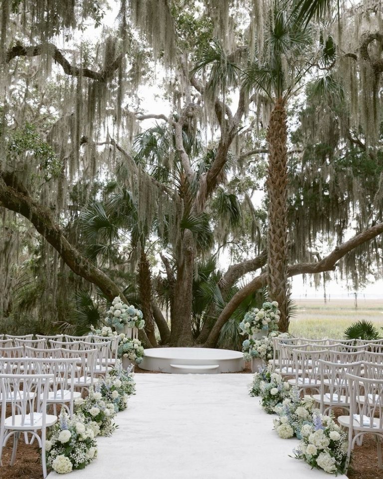 Southern wedding ceremony setup with white hydrangea florals along aisle under moss-covered oaks