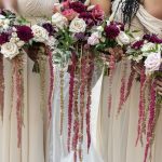 Bridesmaids holding burgundy and blush cascading floral bouquets with ribbon streamers