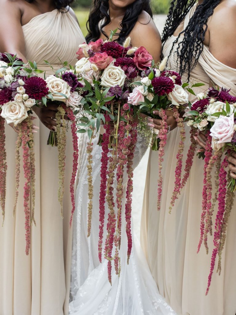 Bridesmaids holding burgundy and blush cascading floral bouquets with ribbon streamers