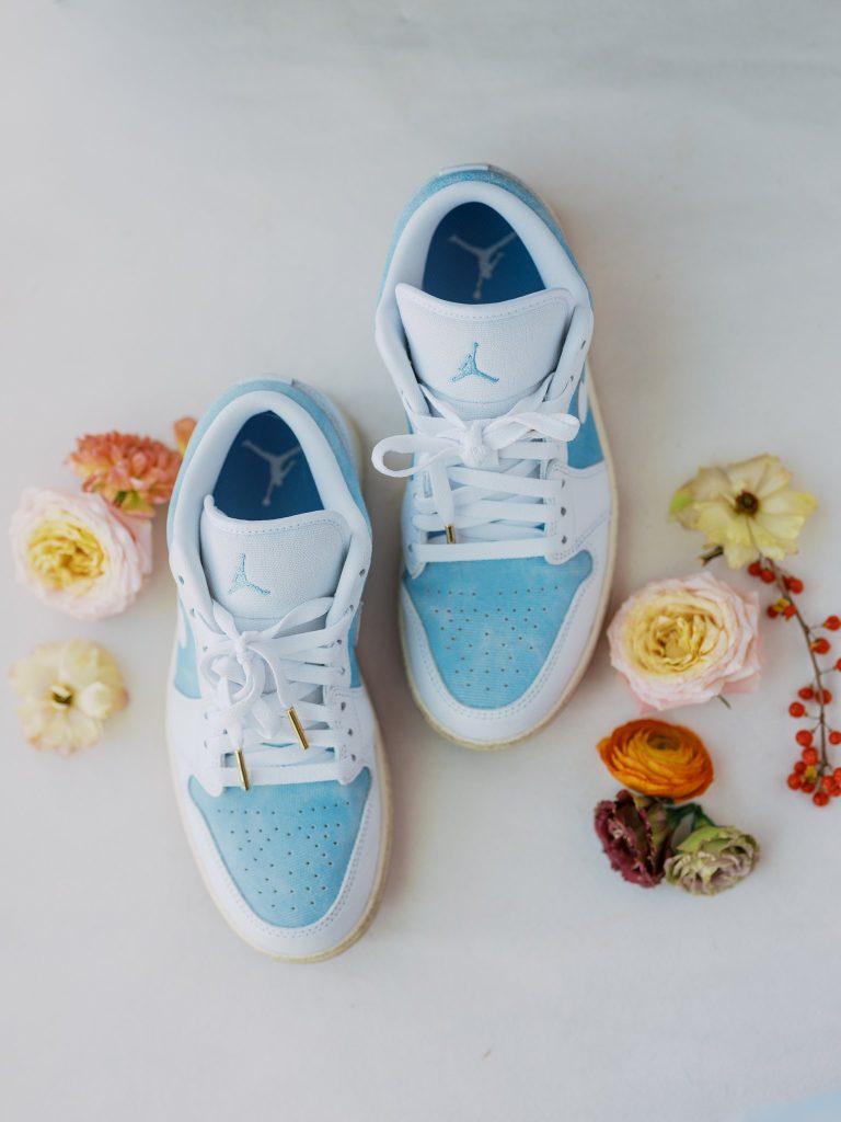 Light blue and white Air Jordan sneakers arranged with pink, yellow, and orange ranunculus flowers