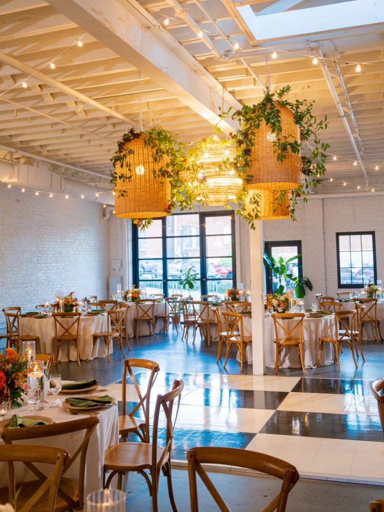 Industrial loft reception space with woven pendant lights, string lighting, cross-back chairs, and checkerboard dance floor