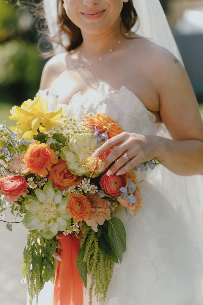 Close-up of bride with cheerful yellow and orange bridal bouquet featuring dahlias, ranunculus, and daisies