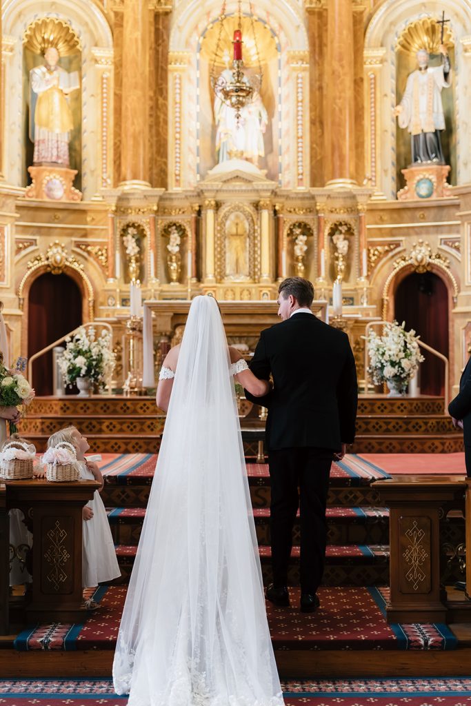 Bride and groom standing at ornate golden altar during their wedding ceremony in French-inspired cathedral