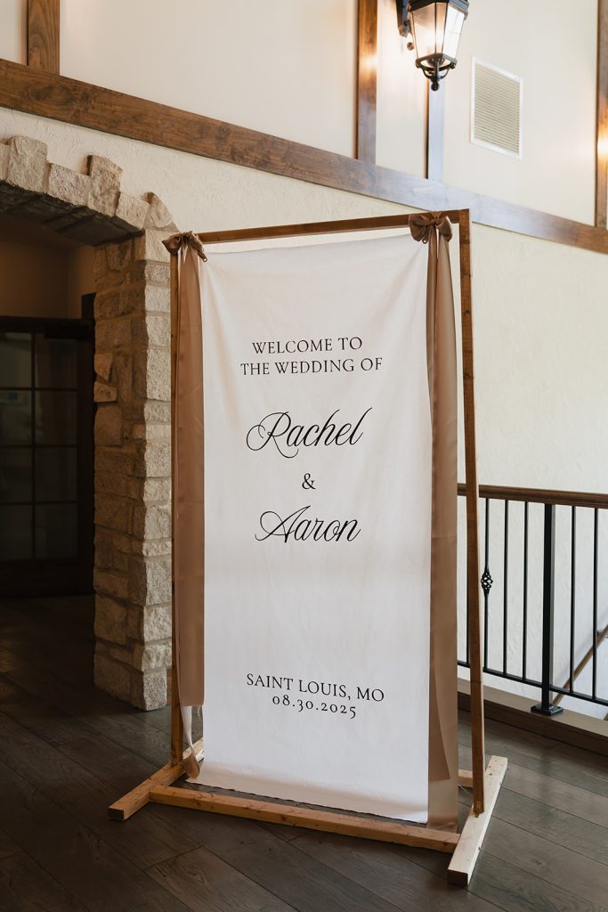 Elegant white fabric welcome sign displaying Rachel and Aaron's names and wedding date in script lettering
