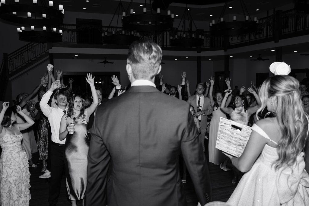 Groom addressing celebrating wedding guests with raised hands on the dance floor