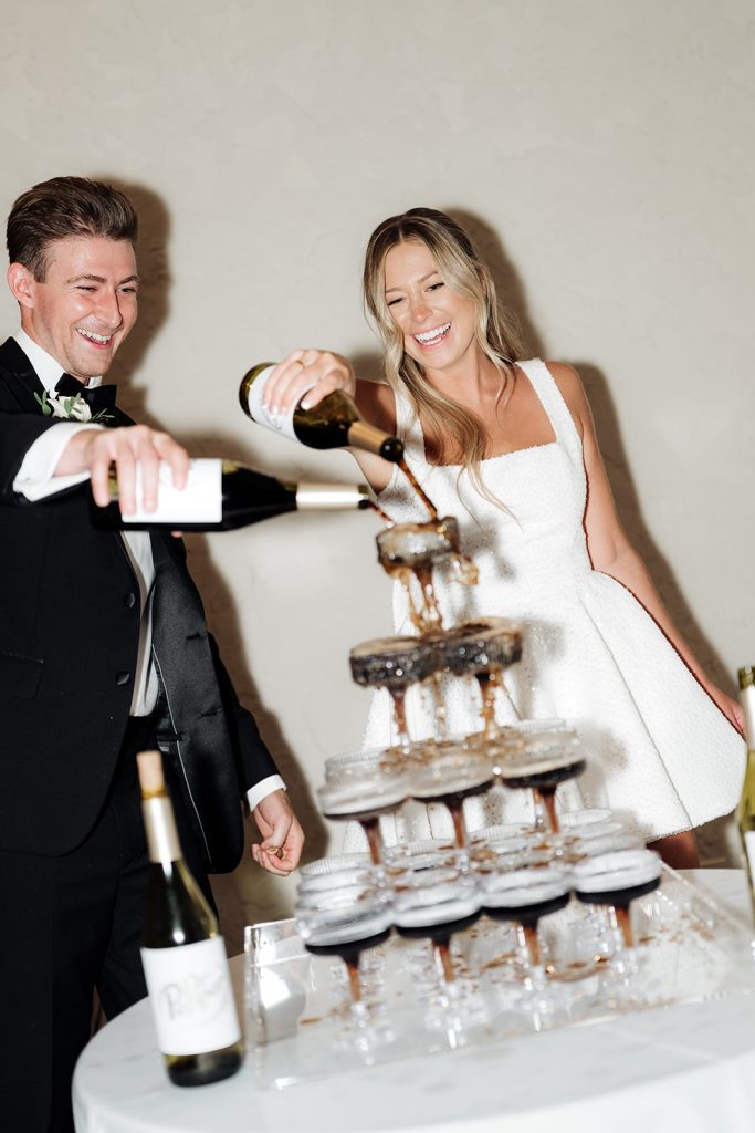 Rachel and Aaron pouring champagne over a tower of coupe glasses during their wedding reception