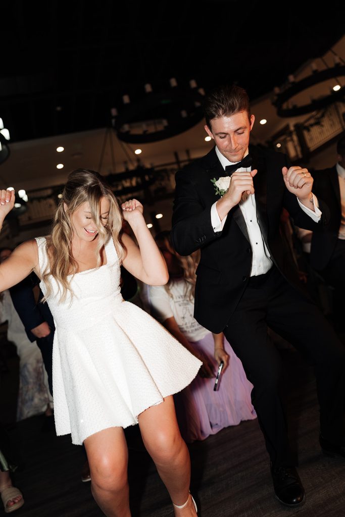 Rachel and Aaron dancing together in reception attire, bride wearing short white party dress