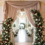 Elegant ceremony aisle with draped fabric and tall floral arrangements flanking the entrance