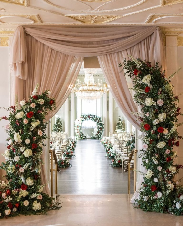 Elegant ceremony aisle with draped fabric and tall floral arrangements flanking the entrance