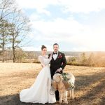 Bride and groom with decorated goat in rustic outdoor setting with rolling hills