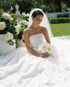 Bride in strapless lace gown holding simple white peony bouquet in garden setting