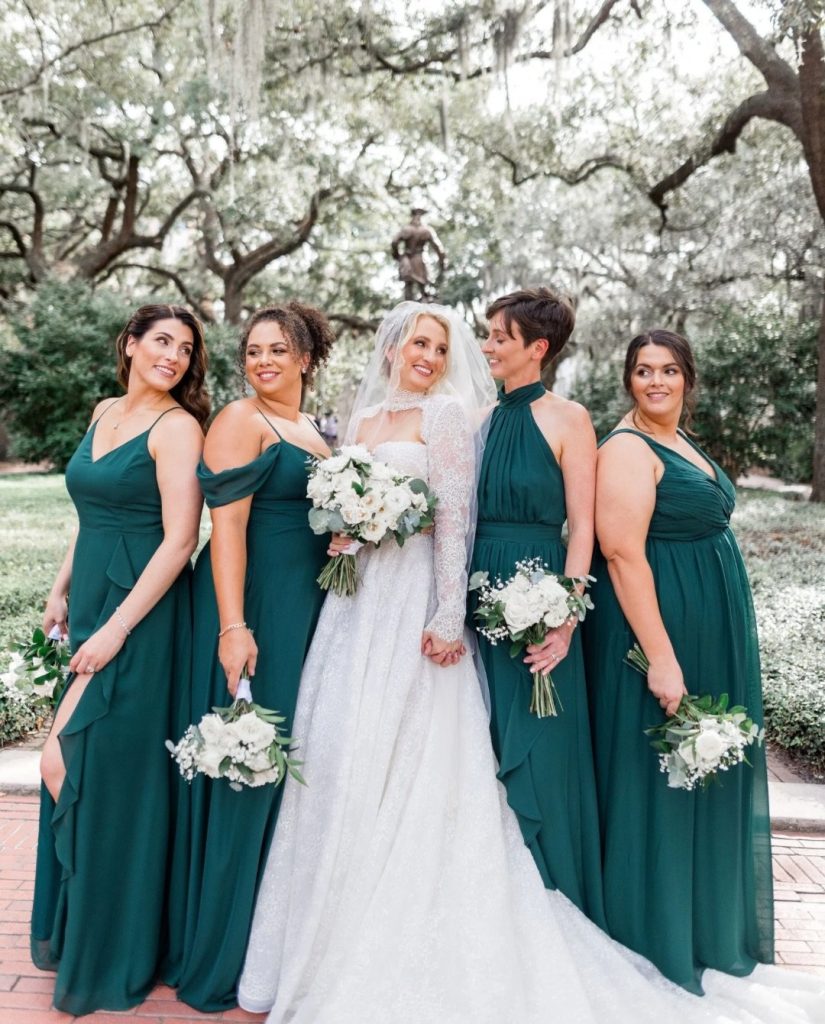 Bride and bridesmaids in emerald green gowns holding white bouquets under Spanish moss-draped oak trees in Savannah