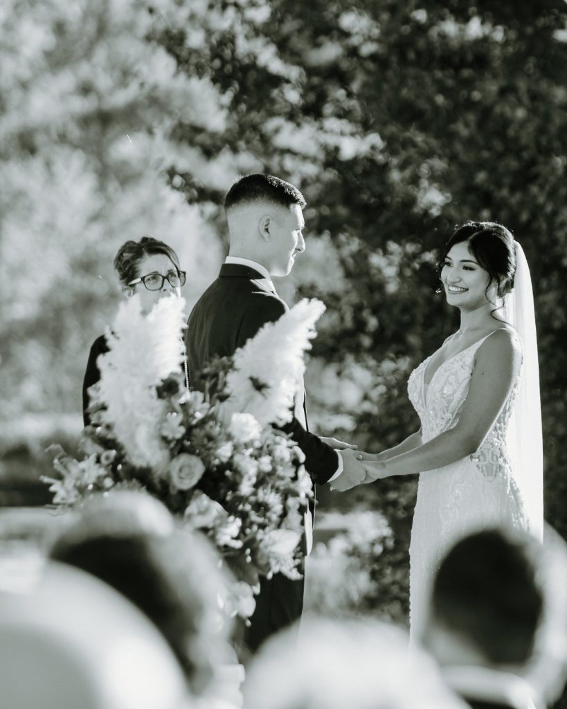 Bride and groom in a grayscale image exchanging vows during wedding ceremony outdoors at King Cole Farm in Dover, Delaware.