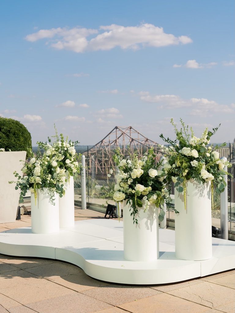 Modern white ceremony altar with tall cylindrical vases filled with white and green florals on rooftop venue
