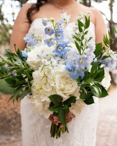 close up shot of bride holding big flower bouquet of blue and white florals with greenery placed throughout